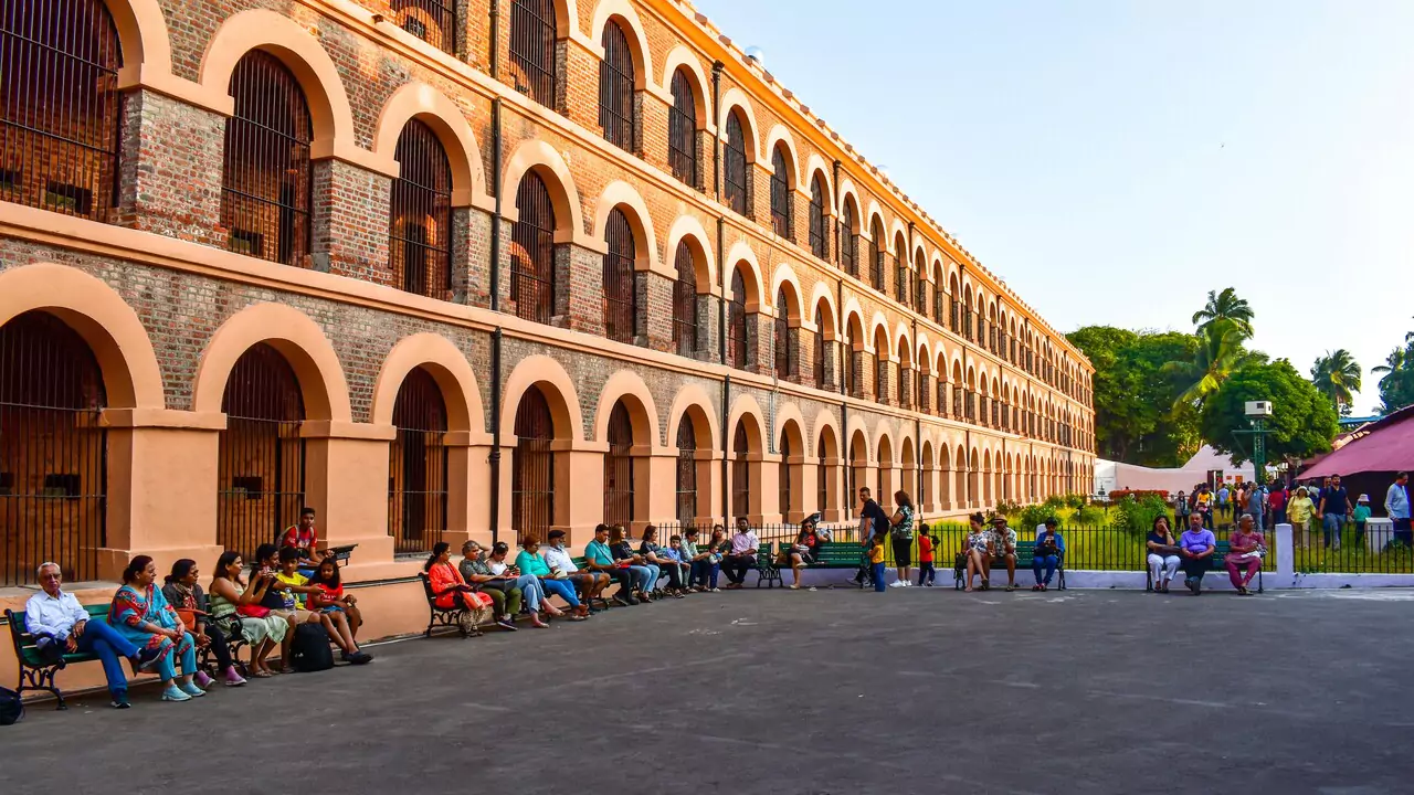 A group of people sitting on benches in front of a cellular jail in port blair, enjoying the outdoors.