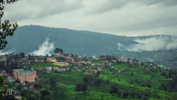 several houses on a hill in almora with mountains in distance