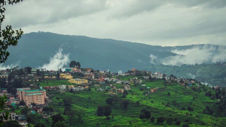 several houses on a hill in almora with mountains in distance