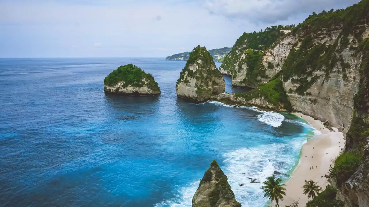 Nusa Lemuro beach in Bali, showcasing soft sand, turquoise waves, and vibrant greenery along the shoreline.