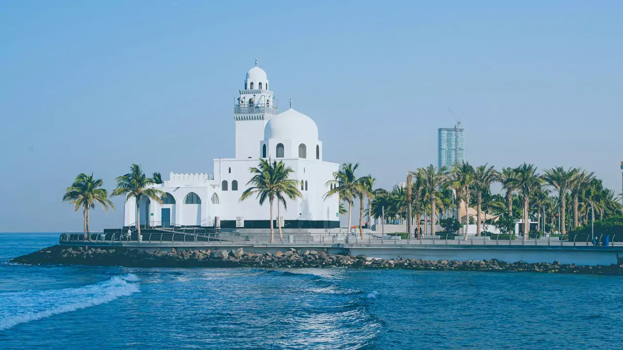 A white mosque by the ocean, surrounded by sand and water, creating a serene coastal scene.