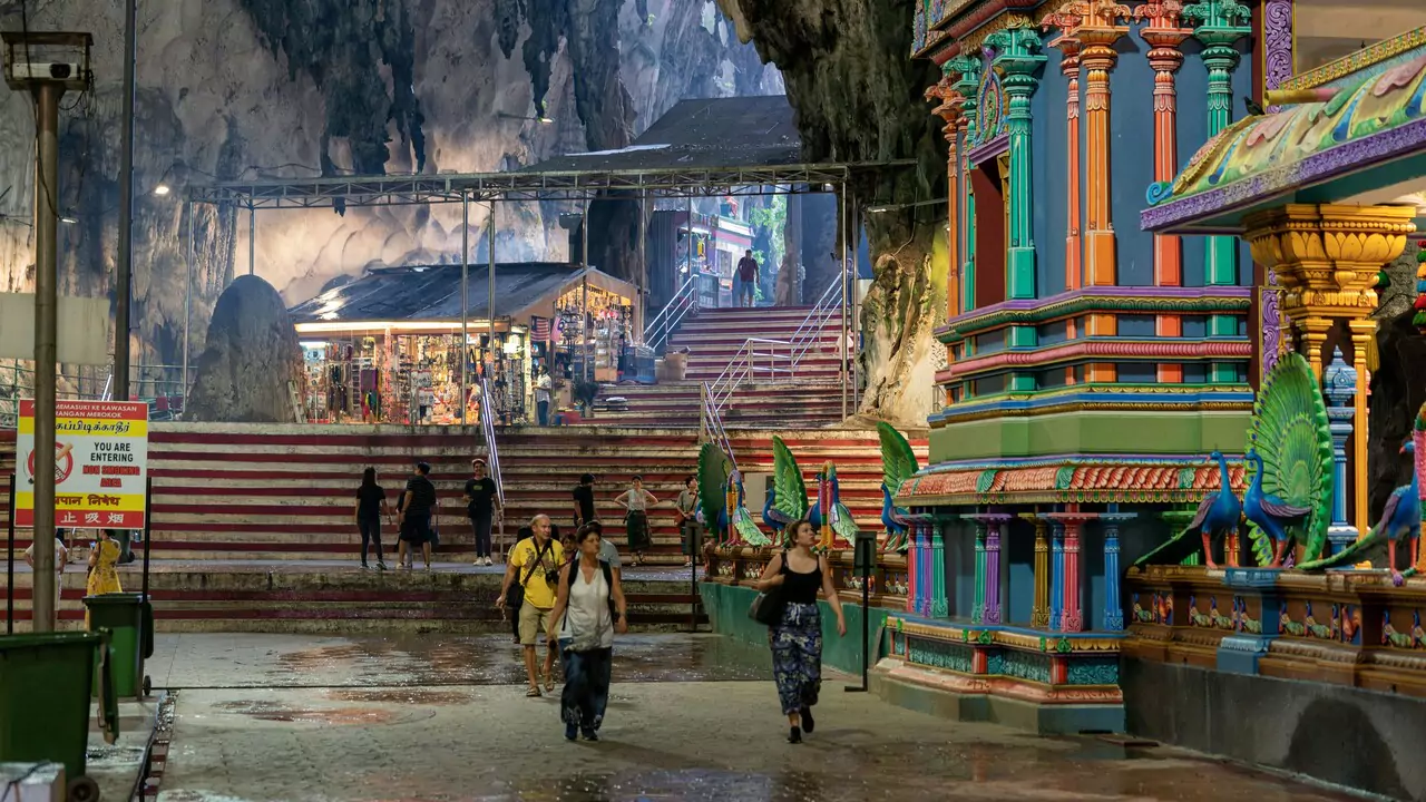 A group of people strolls through a narrow alleyway leading to a temple, in batu caves.