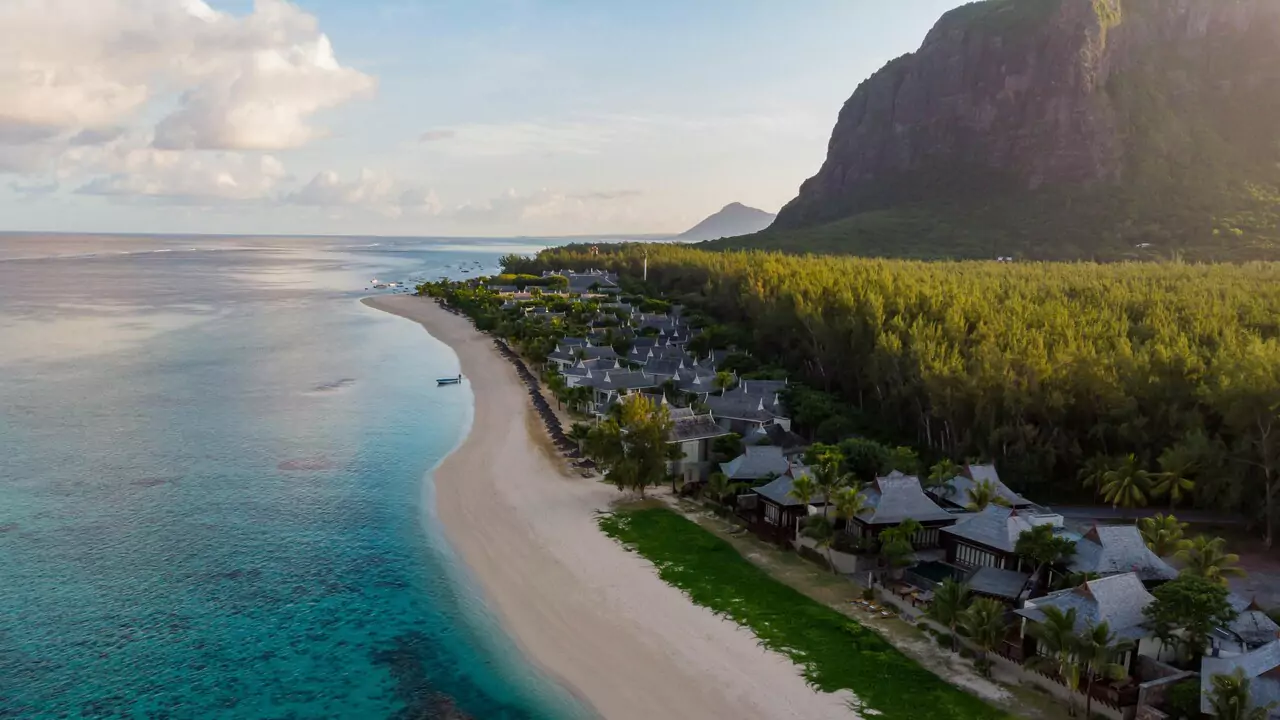Aerial view of a beach resort with palm trees, pools, and sun loungers along the sandy shore.