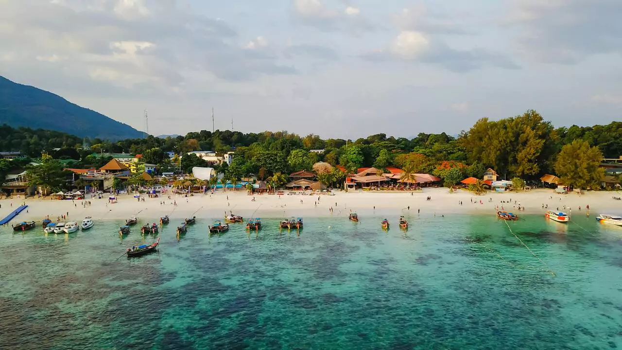 A lively beach with people sunbathing and playing, while boats are moored along the shore.