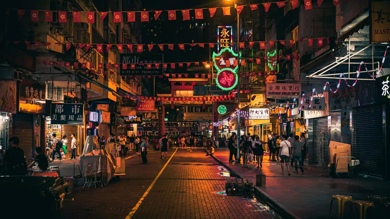 A bustling city street at night, filled with people walking and shopping under bright lights.
