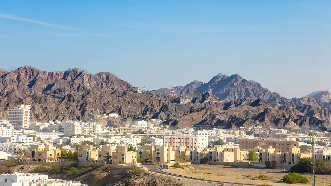 A panoramic view of Oman city, nestled among majestic mountains under a clear blue sky.