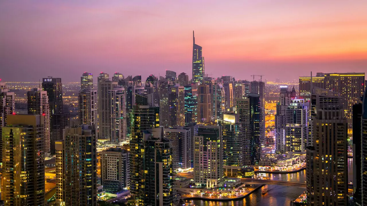 Dubai skyline at sunset, showcasing tall buildings silhouetted against a vibrant orange and purple sky.