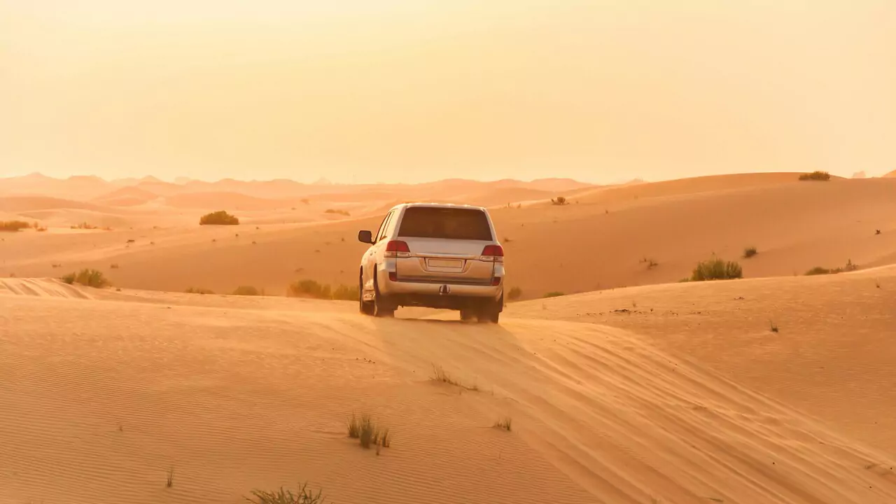 An SUV drives through a desert landscape, surrounded by golden sand.