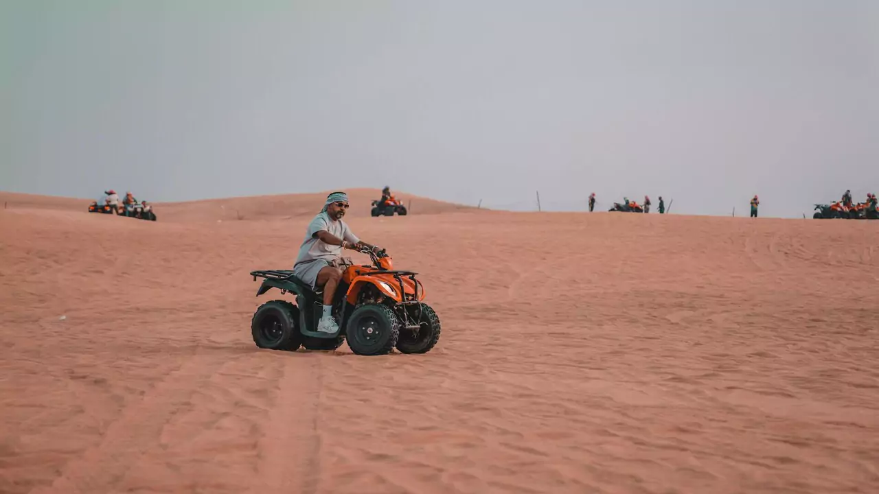 A man riding an ATV across a sandy desert landscape under a clear blue sky.