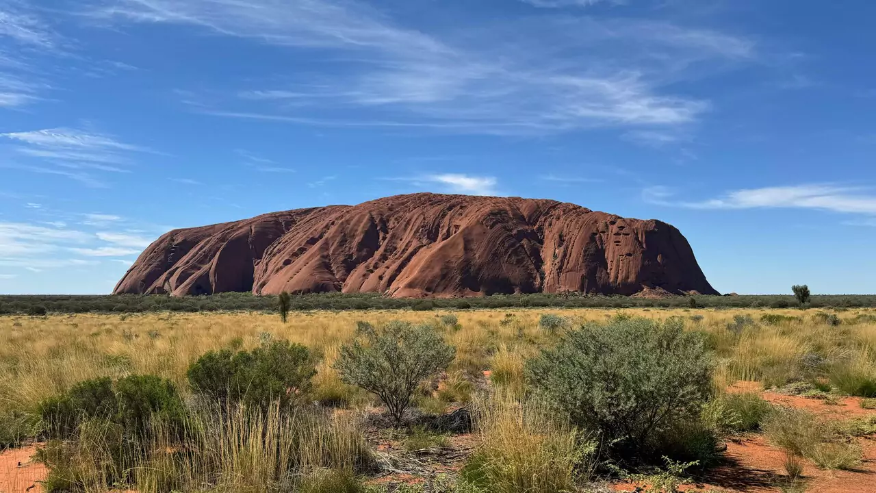 A stunning view of Uluru, a massive sandstone monolith in the Australian desert, surrounded by a clear blue sky.