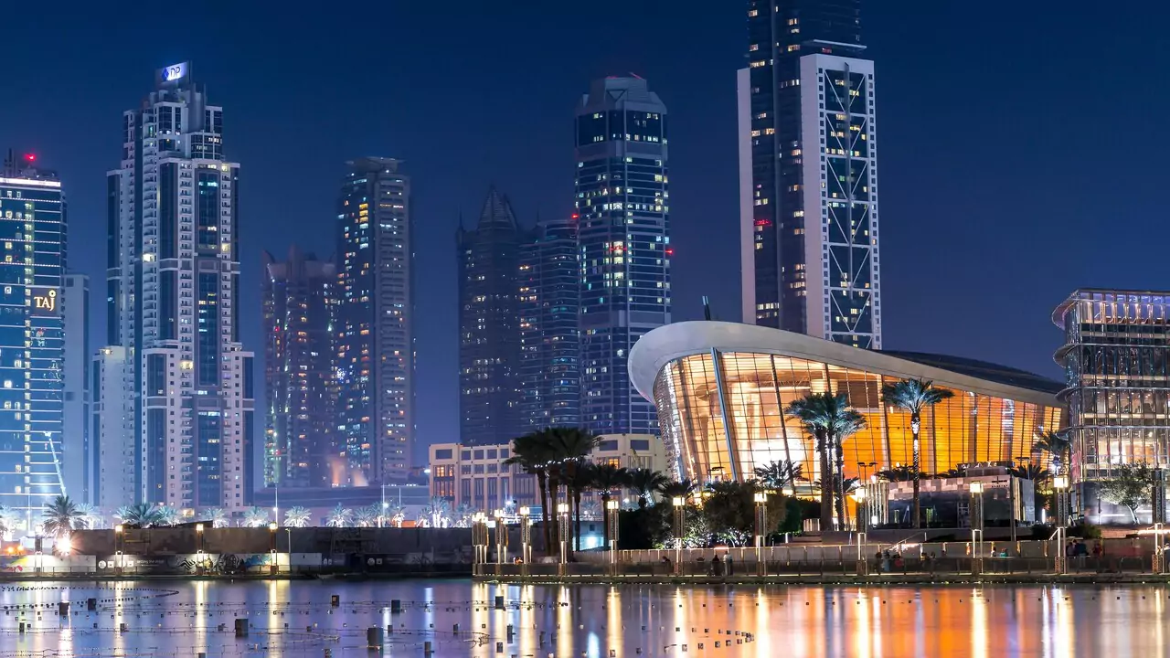 Dubai skyline at night, featuring illuminated opera house and skyscrapers.