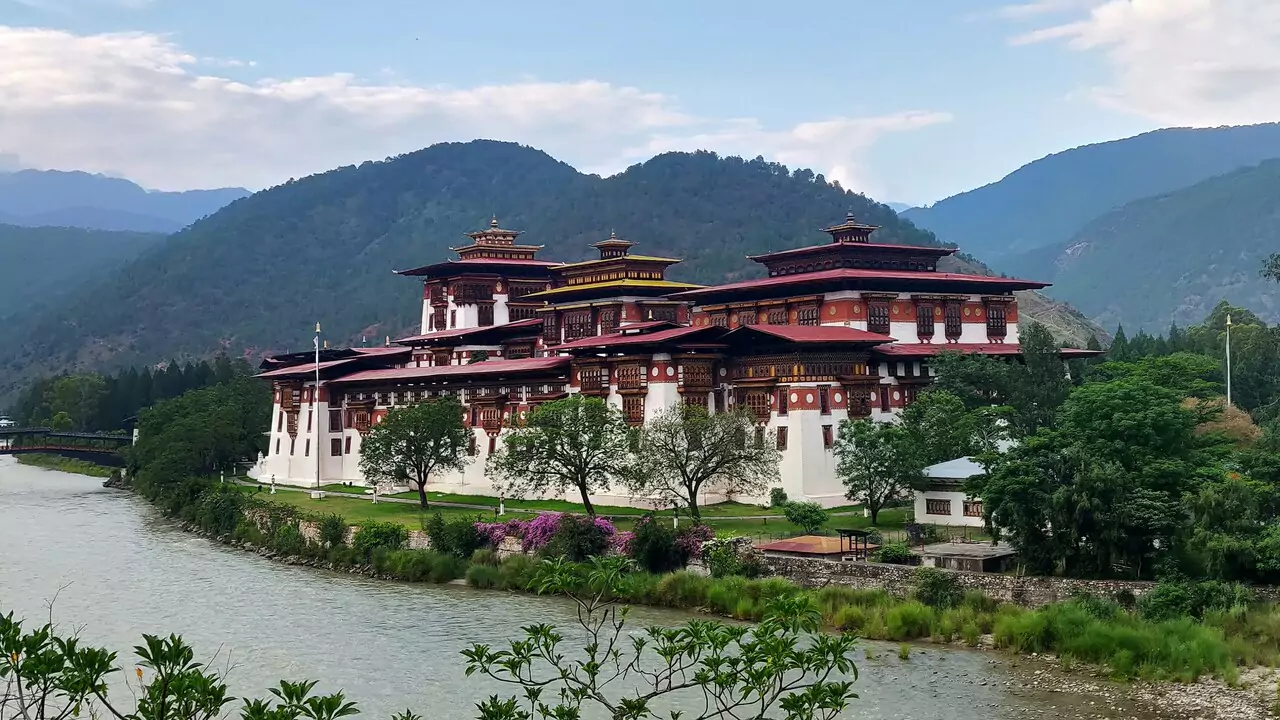 The dzong in Bhutan, featuring intricate designs and surrounded by lush greenery and distant mountains.