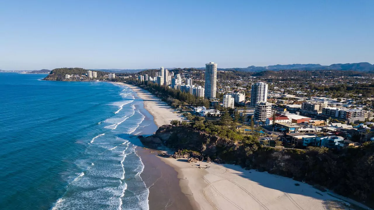  Vibrant Gold Coast beach scene featuring golden sand, turquoise waves, and beachgoers relaxing under the sun.