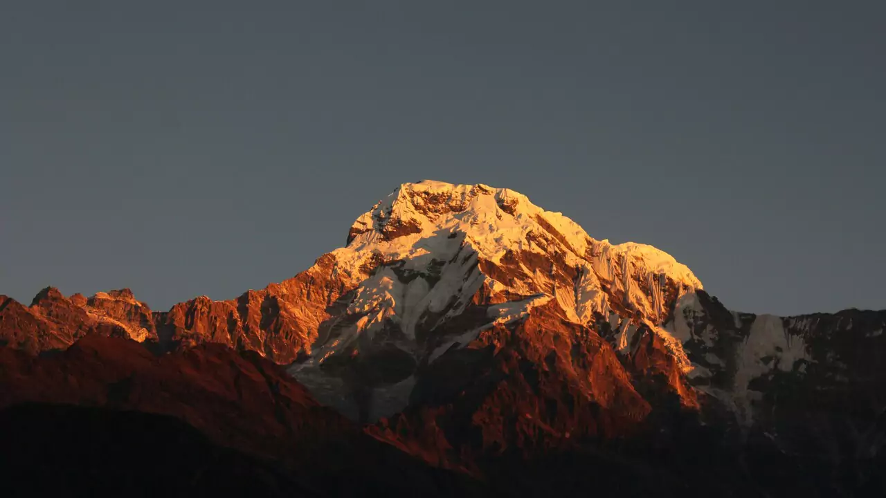 A vibrant sunset casts warm colors over a mountain peak, silhouetting its rugged outline against the colorful sky.