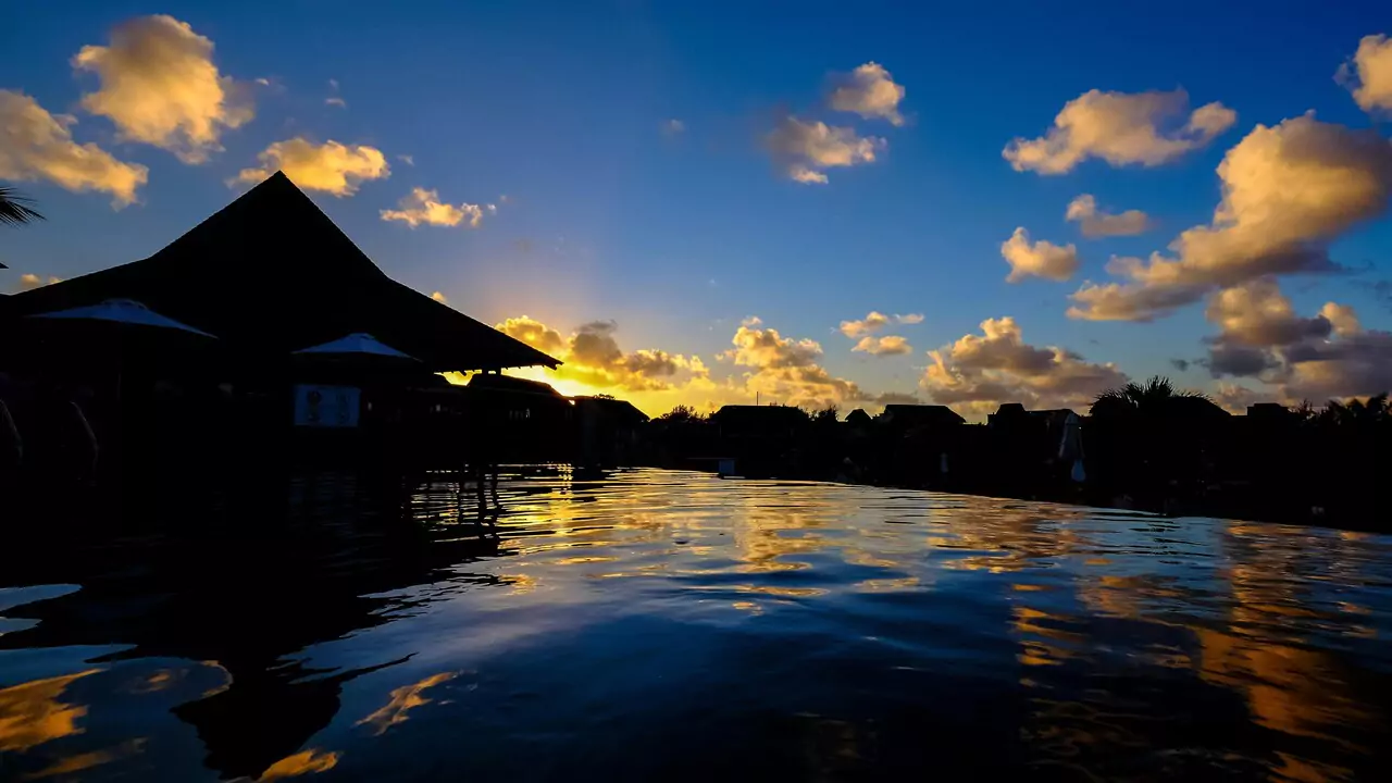 A beautiful sunset reflects on a calm pool, with vibrant colors filling the sky and water.