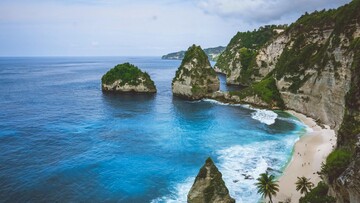 Nusa Lemuro beach in Bali, showcasing soft sand, turquoise waves, and vibrant greenery along the shoreline.