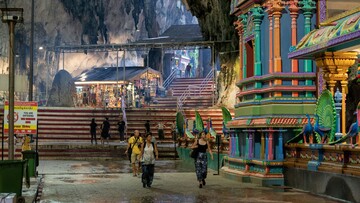 A group of people strolls through a narrow alleyway leading to a temple, in batu caves.