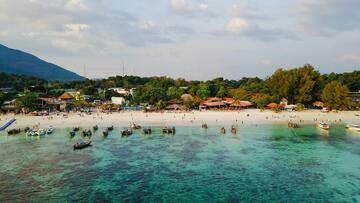A lively beach with people sunbathing and playing, while boats are moored along the shore.