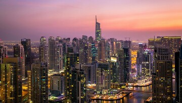 Dubai skyline at sunset, showcasing tall buildings silhouetted against a vibrant orange and purple sky.