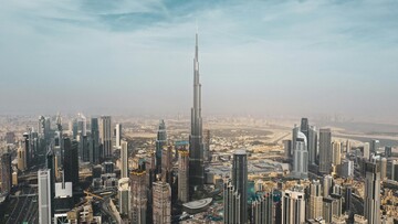 View of Dubai skyline from the top of Burj Khalifa, showcasing tall buildings and the cityscape under a clear blue sky.