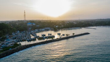 Sunset over a beach and town, captured from above, showcasing colorful skies and calm waves.