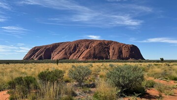 A stunning view of Uluru, a massive sandstone monolith in the Australian desert, surrounded by a clear blue sky.