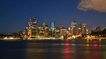 City skyline at night with bright lights reflecting on the calm water below.