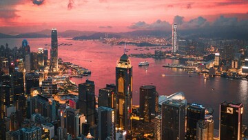 Sunset over Hong Kong skyline, showcasing skyscrapers outlined by vibrant orange and purple clouds.
