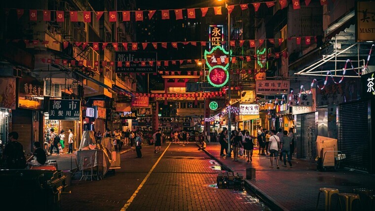 A bustling city street at night, filled with people walking and shopping under bright lights.