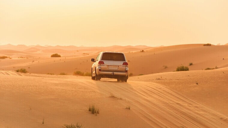 An SUV drives through a desert landscape, surrounded by golden sand.