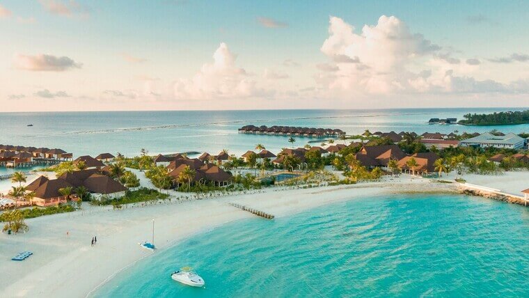 Overhead shot of a Maldives beach resort, featuring clear blue water, sandy shores, and palm trees.