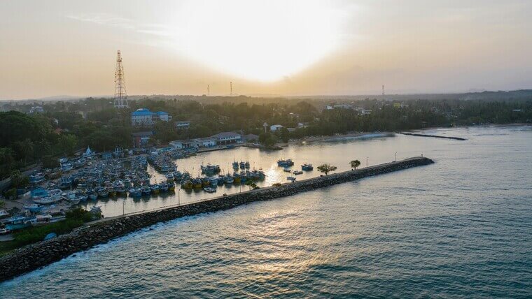 Sunset over a beach and town, captured from above, showcasing colorful skies and calm waves.