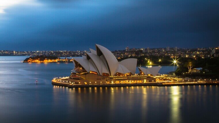 Sydney Opera House illuminated at dusk, showcasing its iconic sails against a colorful evening sky.