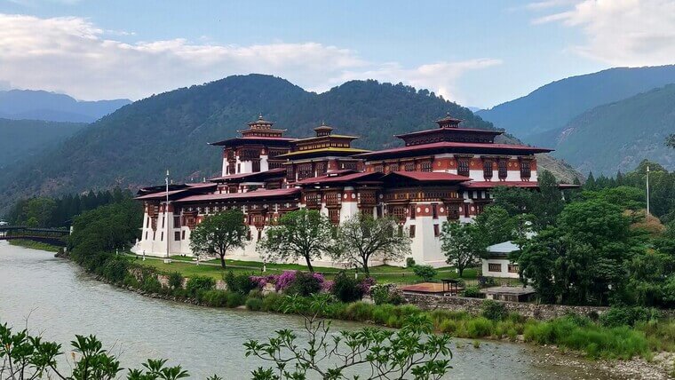 The dzong in Bhutan, featuring intricate designs and surrounded by lush greenery and distant mountains.